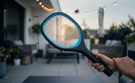 Modern electric swatter with blue accent held on a dusky patio. Its grid glows, surrounded by blurred mosquitoes and a fly.